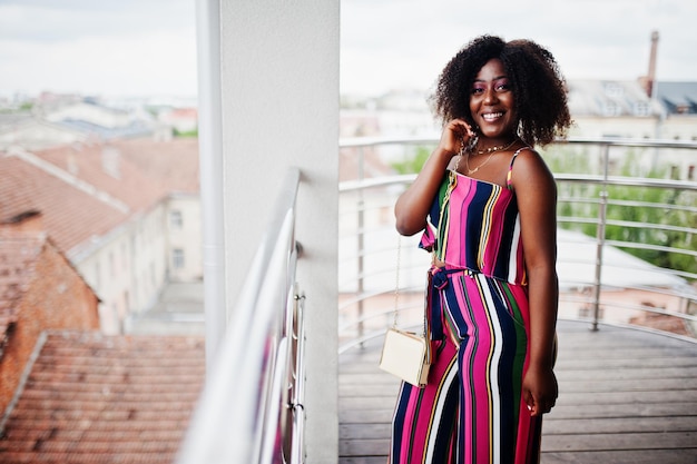 Free photo fashionable african american woman in pink striped jumpsuit with handbag posed in the french balcony