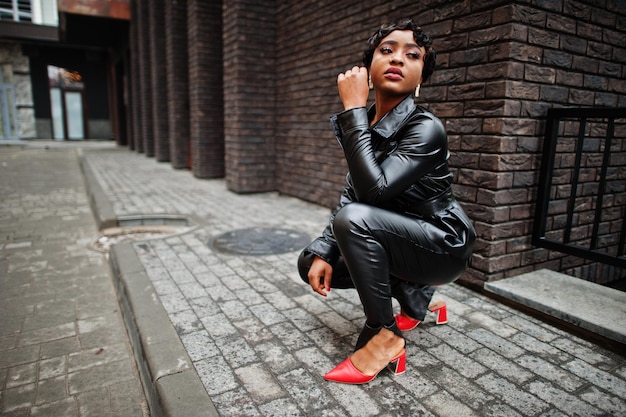 Fashionable beautiful african american woman posing in black leather jacket and pants at street