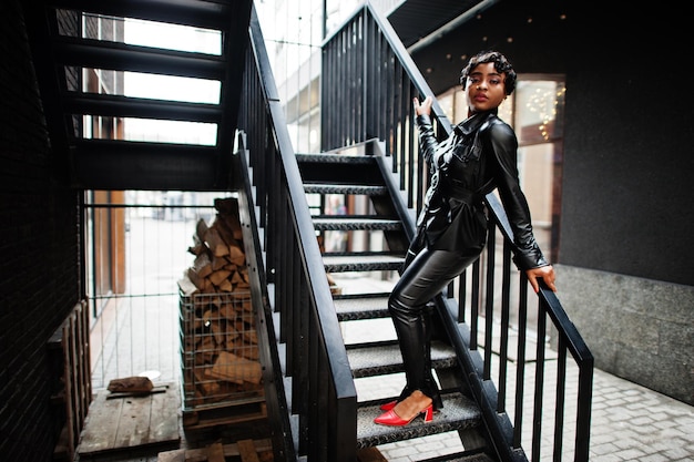 Fashionable beautiful african american woman posing in black leather jacket and pants at street