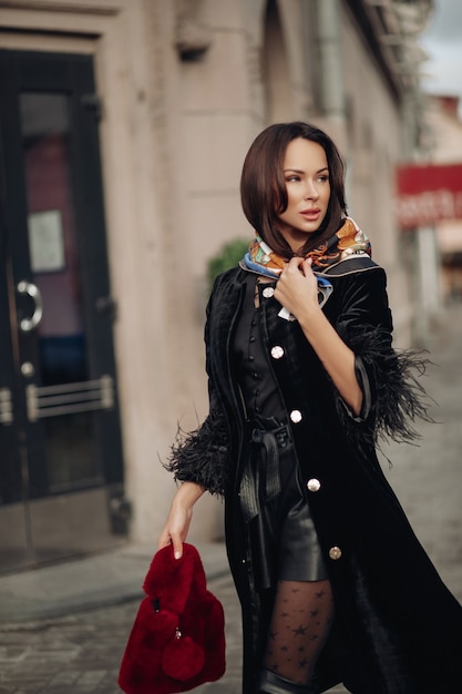 fashionable beauty young woman in trendy clothes walking outdoor at city downtown. beautiful stylish brunette girl in black outerwear posing surrounded by building exterior