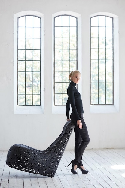 Free photo fashionable blond female posing near artistic black chair.