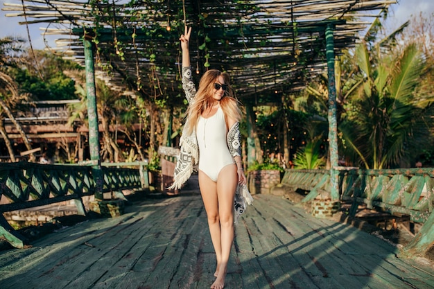 Fashionable blonde woman in white swimwear in exotic place