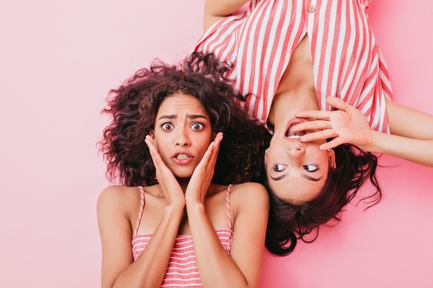 Fashionable and bright girls with beautiful brown eyes and stylish hair, dressed in striped sundresses of soft pink color