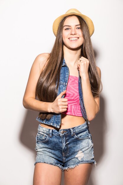 Fashionable brunette woman in straw hat and sunglasses smiling isolated over white wall