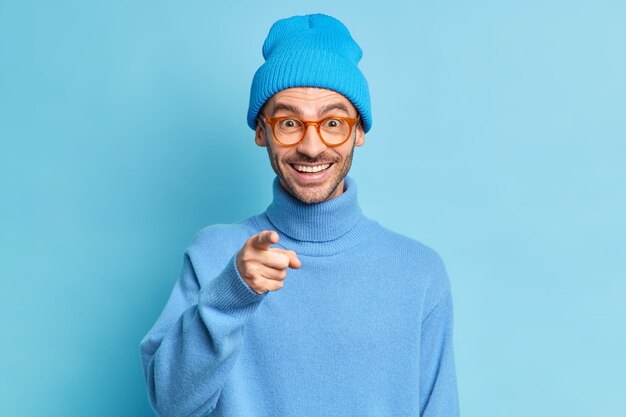 Fashionable cheerful guy with bristle points directly at camera feels glad