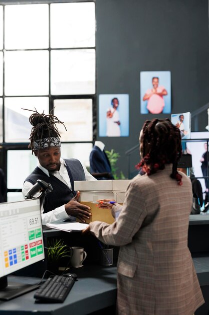 Fashionable customer holding packages fiiled with clothes, paying for merchandise at cash register in showroom. African american client buying stylish fashion collection, commercial activity