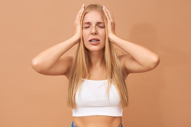 Free photo fashionable cute teenage girl with blonde hair wears jeans and white top suffering from headache