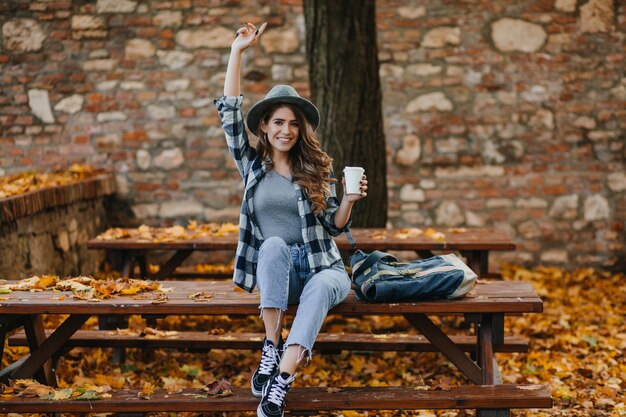 Fashionable girl in short blue jeans sitting with cup of coffee in front of old building