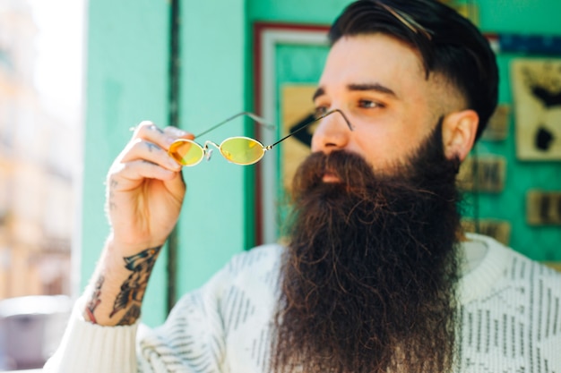 Free photo fashionable handsome young bearded man holding yellow eyeglasses in hand