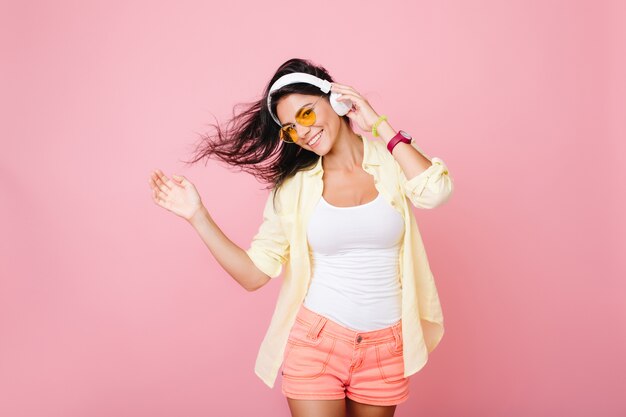 Fashionable latin girl in good mood posing for photo and dancing. Enthusiastic hispanic young lady in summer outfit relaxing while listening favorite song.