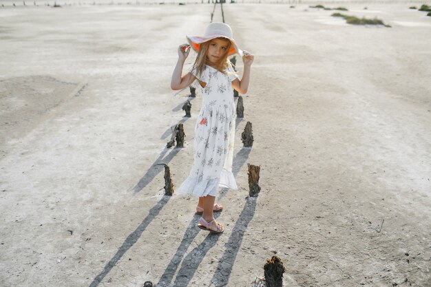 Fashionable little girl model dressed in summer white dress is holding edges of the hat