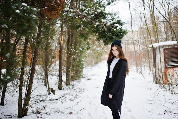 Модная брюнетка с длинными ногами в длинном черном плаще и шляпе на открытом воздухе в зимний день