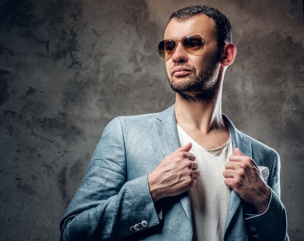 Fashionable male in azure jacket and sunglasses posing in a studio.