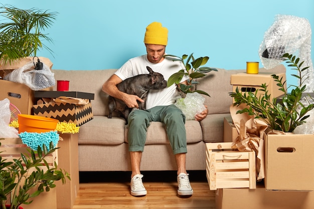 Free photo fashionable man poses on cozy sofa with favourite pet