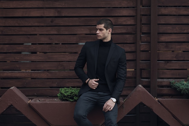 Uomo alla moda, indossa un abito, seduto contro la parete di legno