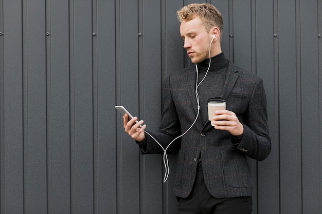 Free photo fashionable man with coffee looking at smartphone