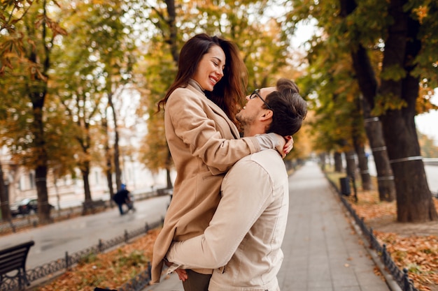 Fashionable man and woman embarrassing while dating in autumn park. Wearing stylish beige coats. Romantic mood.