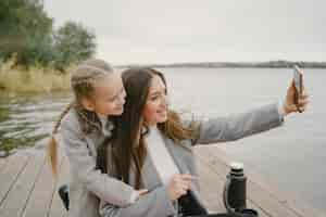 Free photo fashionable mother with daughter. people on a picnic. woman in a gray coat. family by the water.