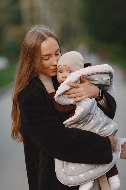 Fashionable mother with daughter. People walks outside. Woman in a black jacket.