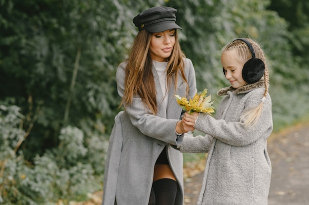 Fashionable mother with daughter. People walks outside. Woman in a gray coat.