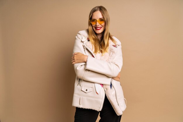 가을 겨울 가을 시즌에 모피 유행 재킷과 화려한 스카프 베이지색 배경을 입은 아름다운 금발 여성의 세련된 스튜디오 초상화