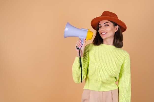 Fashionable stylish woman in full growth   in trousers, a sweater and a hat shouts excitedly into a megaphone