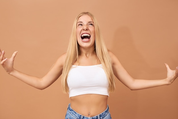 Fashionable teenage girl with blonde hair wears jeans and white top shouting