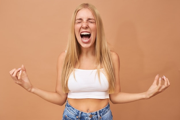 Fashionable teenage girl with blonde hair wears jeans and white top shouting