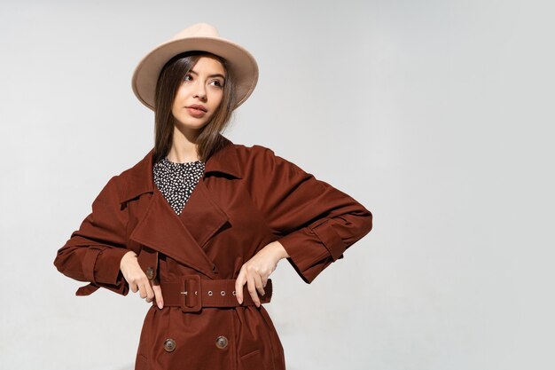茶色のコートとベージュの帽子のポーズでファッショナブルな女性