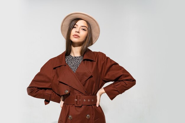 茶色のコートとベージュの帽子のポーズでファッショナブルな女性