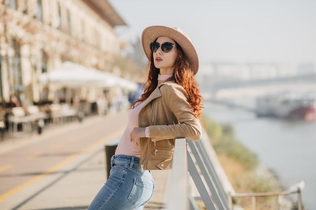 Donna alla moda in jeans casual che gode del servizio fotografico sulla parete del fiume