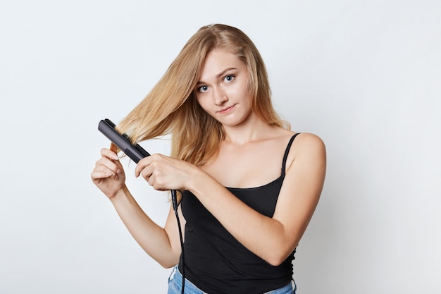 Fashionable woman does hairstyle with hair straightener. Female combs perfect hair with iron. Hair care