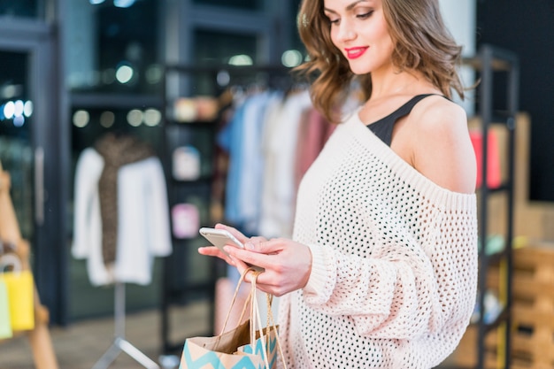 Donna alla moda che esamina il cellulare che tiene i sacchetti della spesa a disposizione