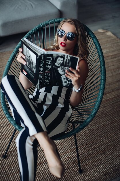 Fashionable woman reading magazine in chair.