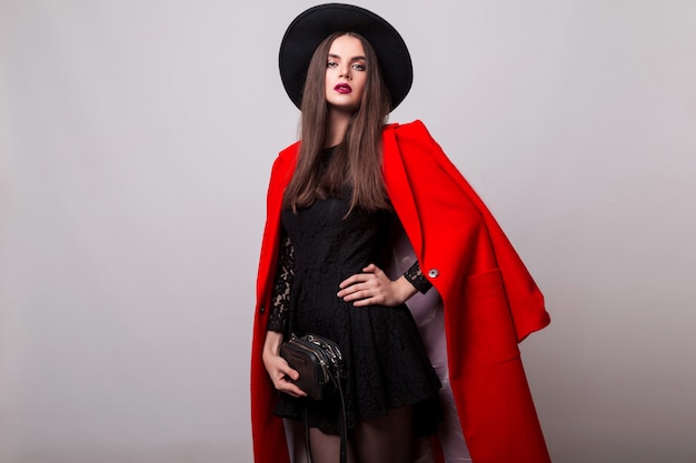 Fashionable woman in red coat and black hat posing