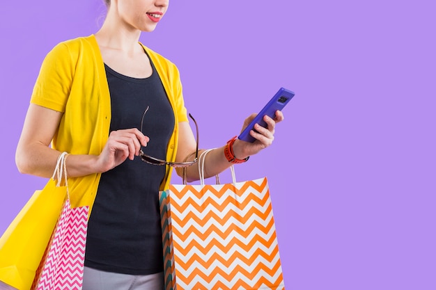 Free photo fashionable woman using cellphone with holding colorful paper bag and eyeglasses