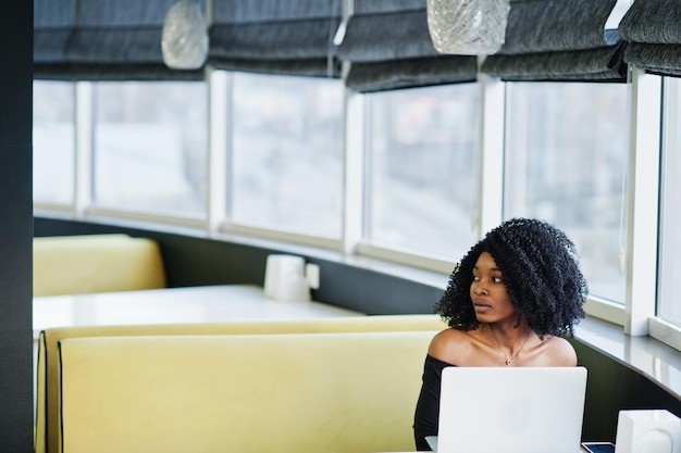 エレガントな黒の座ってラップトップで働くアフロヘアスタイルのファッショナブルな若い美しいアフリカ系アメリカ人のビジネス女性