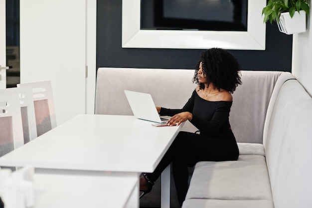 Free photo fashionable young beautiful african american business woman with afro hairstyle wear in elegant black sitting and working at laptop