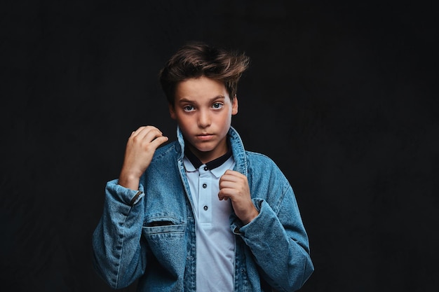 Fashionable young guy dressed in a t-shirt and denim jacket posing in a studio. Isolated on the dark background.