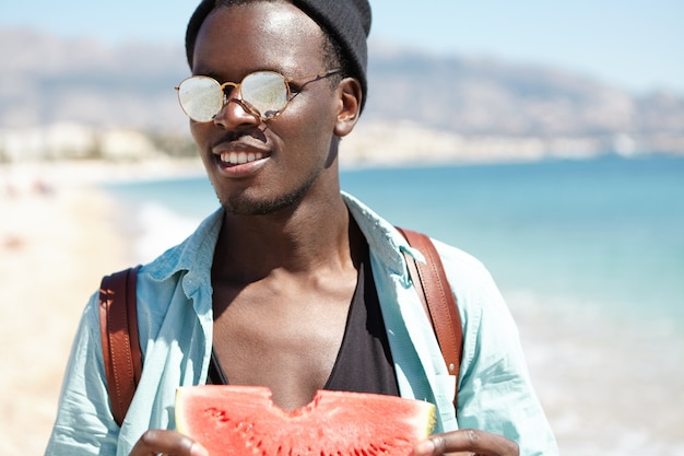 Fashionable young traveler holding slice of sweet ripe watermelon