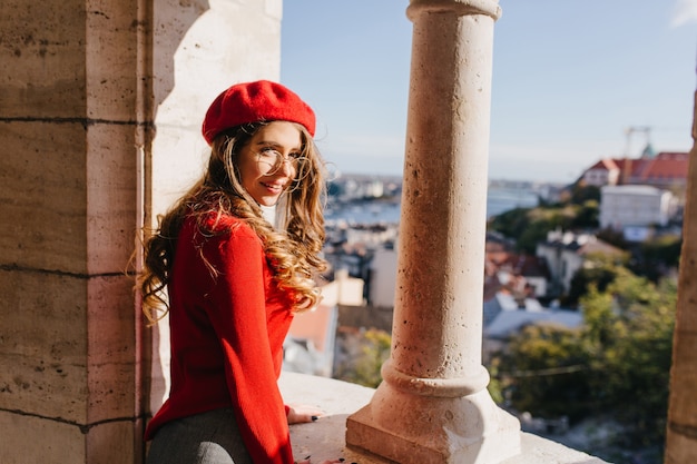 Модная молодая женщина в красной вязаной одежде, наслаждаясь видом на город из старого замка