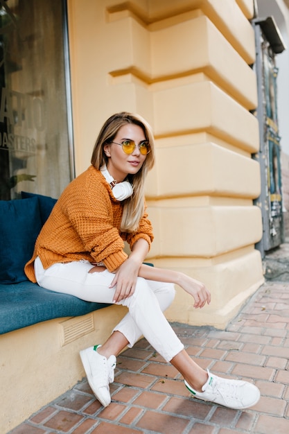 Fashionable young woman in leather sneakers resting after trip around city and looking to camera