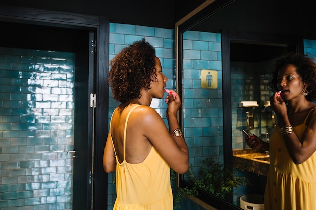 Fashionable young woman looking in mirror applying lipstick