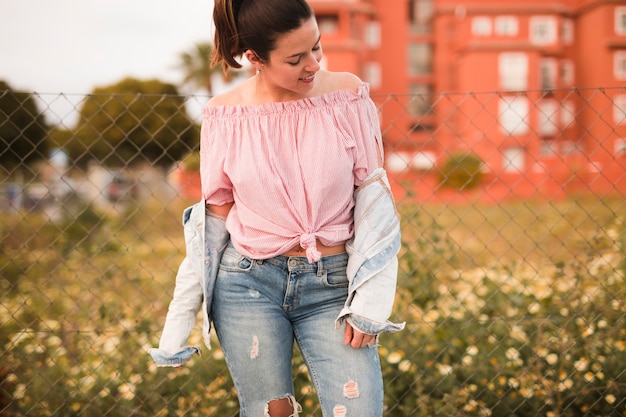 Fashionable young woman standing in front of fence looking away