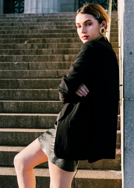 Fashionable young woman standing in front of staircase with arm crossed