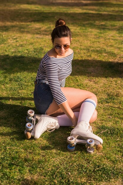Fashionable young woman wearing roller skate sitting on green grass