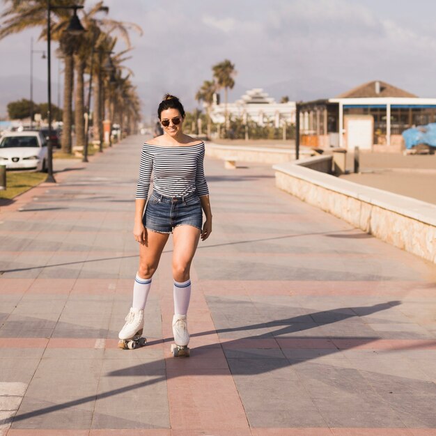 Катание на роликовых коньках модной молодой женщины нося на тротуаре в городе