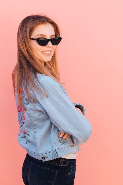 무료 사진 분홍색 배경에 어깨 너머로 보이는 선글라스를 착용하는 유행 젊은 여자