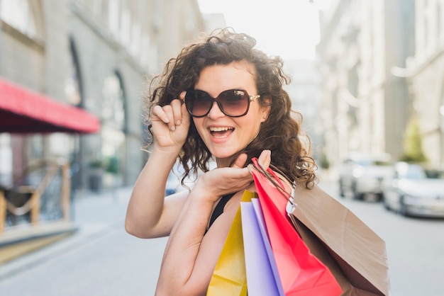 Foto gratuita giovane donna alla moda con gli occhiali da sole che trasportano i sacchi di carta