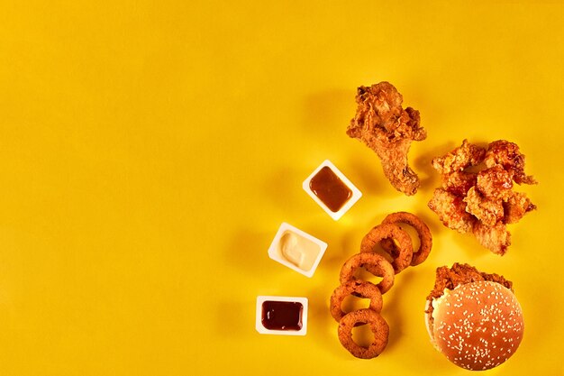 Fast food and unhealthy eating concept - close up of fast food snacks on yellow background. Top view. Copy space. Still life. Flat lay.